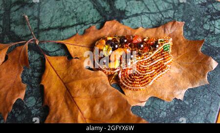 Women's Brooch in the form of an autumn leaf lies on dried yellow oak leaves. Vintage decoration autumn background. Stock Photo