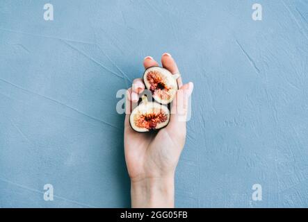 Fresh ripe figs in hand on blue background, close-up. Stock Photo
