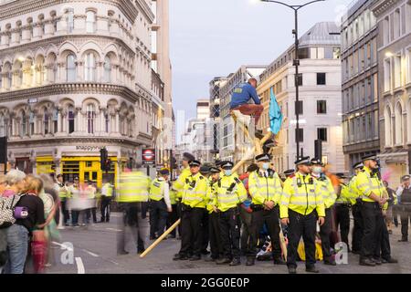 London, UK. 27th August 2021. Extinction Rebellion (XR) and animal rebellion protesters tour the London financial district , square mile, into the night, occupy the mansion house junction of queen Victoria street and cannon street, all the way Bank of England, against Global climate change. climb atop of wood structures erected in the middle of road. To protest against investment in the fossil fuels.  protestors sit on road watching protestors sitting atop bamboo structure .   Credit: Xiu Bao/Alamy Live News Stock Photo