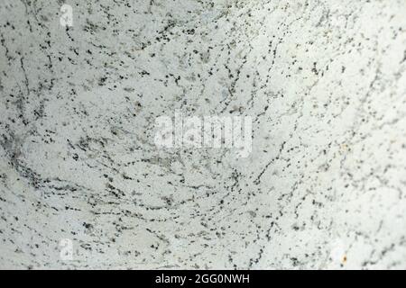 The texture of white stone with inclusions of black dots and lines. The surface of the rock is in detail. Decorative stone in natural light. Stock Photo