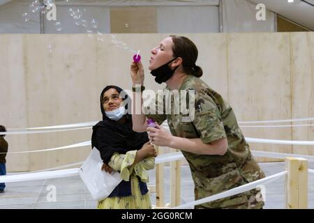 A U.S. Army National Guard Soldier with Task Force Spartan, U.S. Army Central, entertains an Afghan girl with bubbles as she waits to in-process at Camp Buehring, Kuwait, Aug. 23, 2021. U.S. Army Soldiers continue to work with their U.S. Central Command and Department of State teammates to support Afghanistan evacuation efforts with transportation, security, logistics and medical assistance at locations in Kuwait. (U.S. Army Photo by 1st Lt.  James Mason) Stock Photo