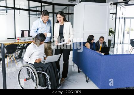 Mexican transgender woman in wheelchair working with coworkers using computer in modern office in Mexico City Stock Photo