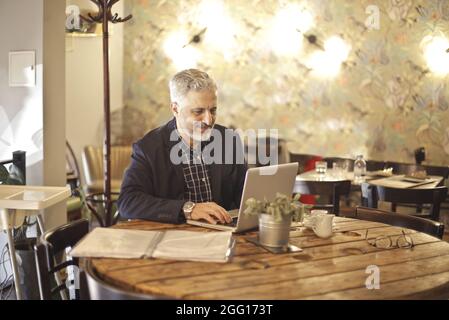 Elder Hungarian using a laptop inside a restaurant Stock Photo