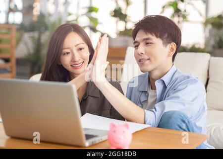 Young couple giving high five and using laptop at home. Stock Photo