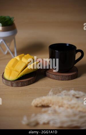 pieces of mango shaped like a blooming flower. fresh fruit and black cup on wooden background, Stock Photo