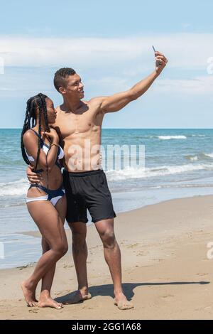 Couple taking selfies with a mobile phone while enjoying a day at the beach. Stock Photo