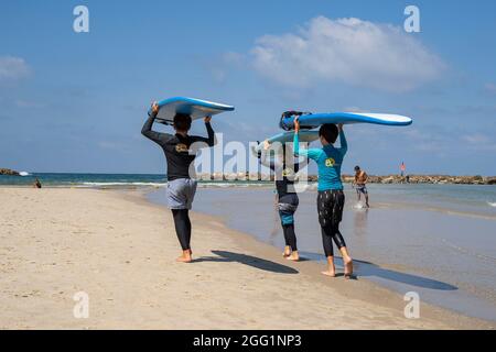 Tel Aviv, Israel - August 15th, 2021: Three young surfers, holding their boards over their heads, heading for sea in Tel Aviv. Stock Photo