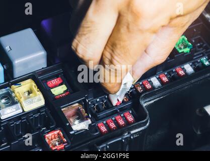 Mechanic replaces the spare fuse to the car fuse box with the fuse clip tool Stock Photo
