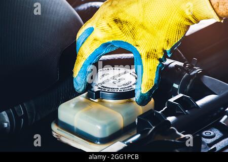 The mechanic hand is open or close the cap of the power steering fluid to check the hydraulic fluid level Stock Photo