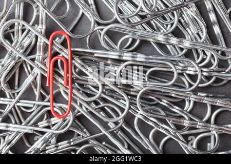 A red paper clip stands out against a textured background of silver paper clips. Concept Stock Photo