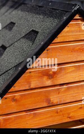 The facade and roof of the dog kennel. Wooden doghouse covered with asphalt shingles. Close-up, selective focus. Stock Photo