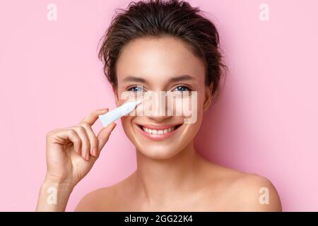 Beautiful woman using cream around the eyes. Photo of woman with perfect makeup on pink background. Beauty and skin care concept Stock Photo