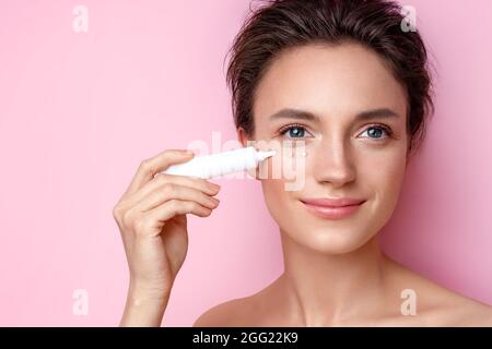 Beautiful woman using cream around the eyes. Photo of woman with perfect makeup on pink background. Beauty and skin care concept Stock Photo