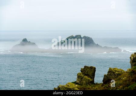 The Brison Islands Shrouded In Mist - View From Cape Cornwall  With A Fishing Boat In Front Which Gives Scale - England UK Stock Photo