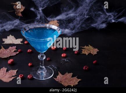 Halloween composition with festive drink, blue cocktail and mini pumpkins, spider web and fallen leaves on black background, selective focus Stock Photo
