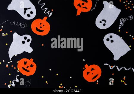 Festive black background on Halloween. White ghosts and orange pumpkins with serpentine lie on a black background, copying space, black layout Stock Photo