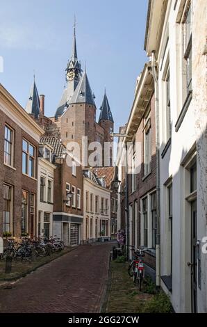 Zwolle, The Netherlands, August 9, 2021: Narrow street in the old town with the tower of Sassenpoort gate rising above the brick and plaster facades Stock Photo