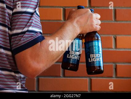 In this photo illustration, man holds Bud Light beer bottles on the background of breek wall. This beer is produced by Anheuser-Busch, ink. Stock Photo