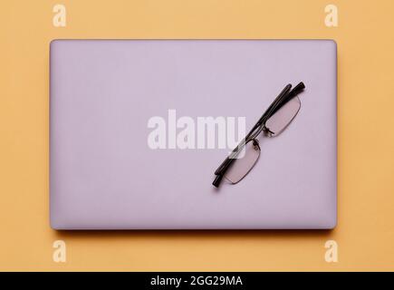 Modern silver closed laptop computer with eyeglasses on top on yellow background Stock Photo