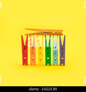 Colorful wood clothespins in different summer colors isolated on trendy yellow background. Multicolor layout and pop art style. Creative community con Stock Photo