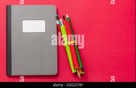 School supplies, Grey color notebook and pencils  on red color background, top view, copy space, template. Education, Back to School, kids creativity Stock Photo