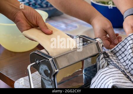 Fresh pasta homemade preparation. Hands working in the kitchen, pasta maker machine and dough closeup view Stock Photo