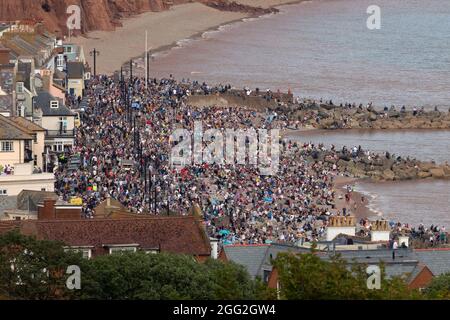 Sidmouth, Devon, UK. 27th Aug 2021.  Members of the public pack the seafront at Sidmouth in Devon to watch a spectacular display performed by the RAF Red Arrows. Credit: Ian Williams/Alamy Live News Stock Photo