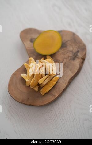 Freeze-dried mango with fresh one on olive wood board , shallow focus Stock Photo
