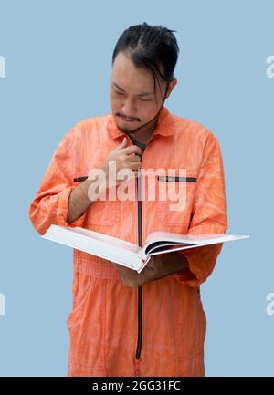 The chief mechanic in an orange uniform holding big book. Stand and read the maintenance manual carefully. Portrait with studio light. Stock Photo
