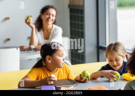 multiethnic kids having lunch in school canteen near teacher smiling on  blurred background Stock Photo - Alamy