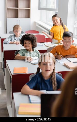 smiling asian schoolgirl talking during lesson near multicultural classmates Stock Photo