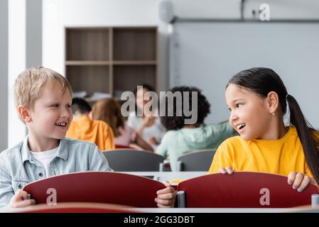 smiling interracial pupils talking during lesson in classroom Stock Photo
