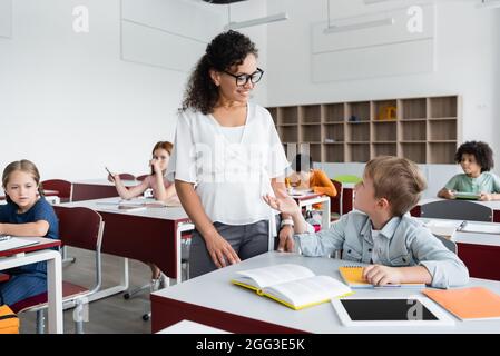 schoolboy gesturing while talking to african american teacher during lesson Stock Photo