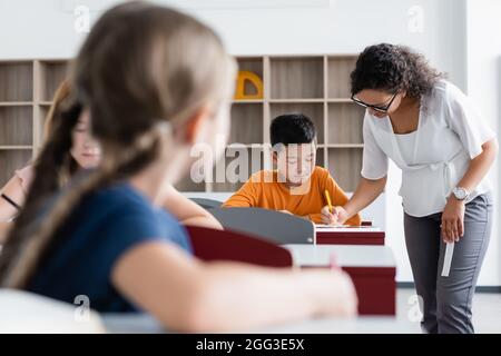 african american teacher helping asian boy during lesson in classroom Stock Photo