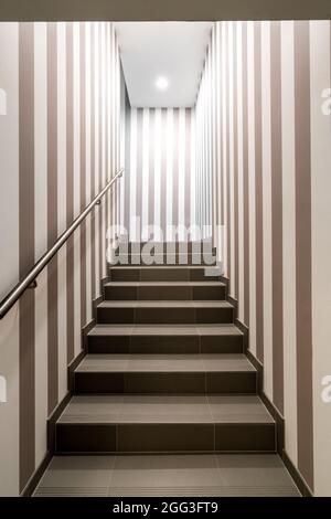 Vertical shot of gloomy lit staircase with vertical dark and white stripes on the walls. Concept for maze, labyrinth, mystery, secret chamber. Stock Photo