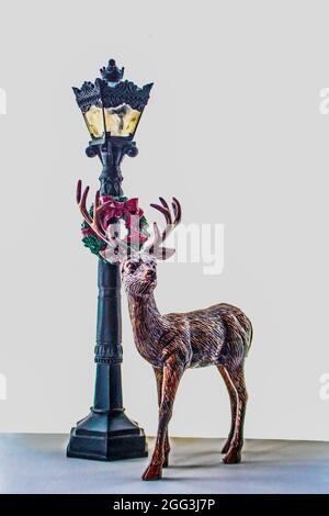 Deer figurine standing by retro Christmas lampost with wreath in front of white background - Room for copy. Stock Photo