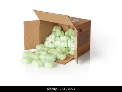 Shipping peanuts spilling out of the parcel box laying on its side, isolated on a white. Brown cardboard box with loose green foam fillers to protect Stock Photo
