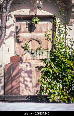 Rustic door with Christmas ornaments and delivered boxes sitting on porch by holly bush Stock Photo