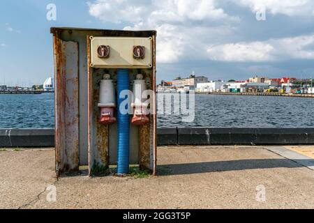 Detail of massive old outdoor electric sockets on concrete harbor pier with port of Hel, Poland, in the background. Electricity for naval vessels Stock Photo