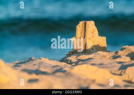 A small sand castle tower built on a beach with blue sea tide in the blurred background on early summer morning. Fun at the Baltic coast in Hel Stock Photo