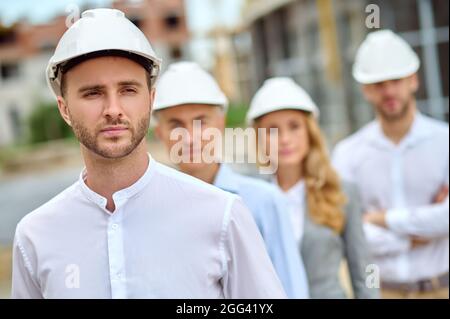 Serene construction worker and his three coworkers wearing protective helmets Stock Photo