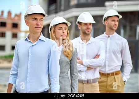 Four adult people in hardhats standing on the building site Stock Photo