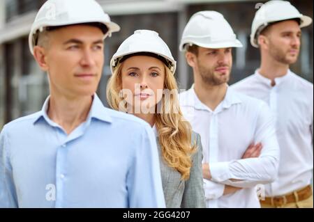 Woman supervisor and builders in hardhats standing outdoors Stock Photo