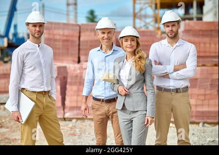 Confident lady supervisor and workers in hardhats standing outside Stock Photo