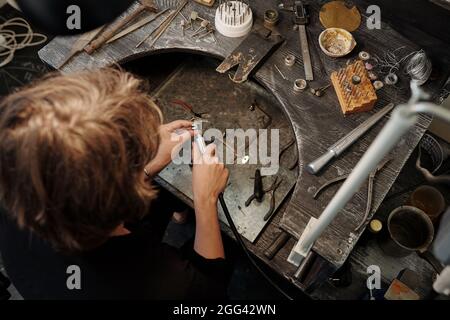 High angle view of jeweler using abrasive tool while polishing silver ring on work station Stock Photo