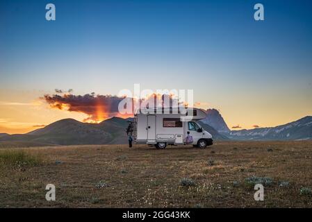 Sunset dramatic sky over camper van in Campo Imperatore highlands, Abruzzo, Italy. Epic clouds above unique highlands and rocky mountains landscape, a Stock Photo