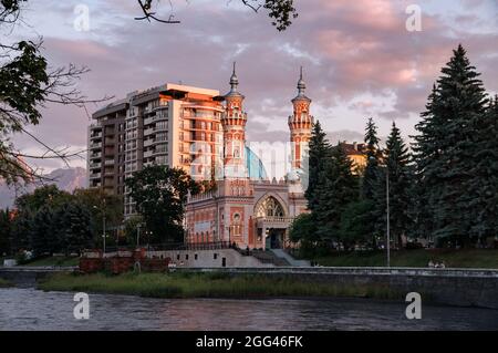 View on Minarets of Sunni Mukhtarov Mosque lit with warm sunset rays in front of pink gray clouds of summer evening sky on the bank of Terek river in Stock Photo