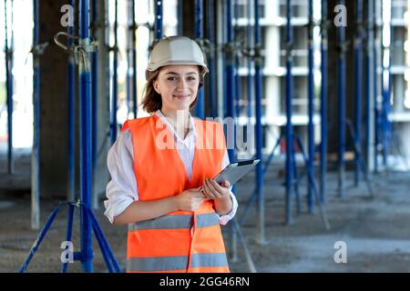 Female construction engineer. Architect with a tablet computer at a construction site. Young Woman looking, building site place on background. Construction concept. Stock Photo