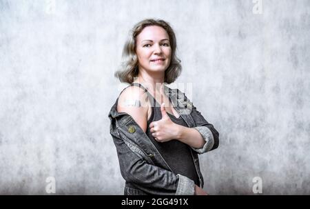 Vaccinated young woman showing arm with plaster. Happy person thumb up after getting coronavirus vaccine. Concept of people COVID-19 vaccination, inje Stock Photo