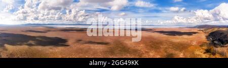 Flat dry dirt soil of Lake George in NSW, AUstralia with windfarm of renewable energy generation wind turbines under cloudy blue sky - aerial panorama Stock Photo